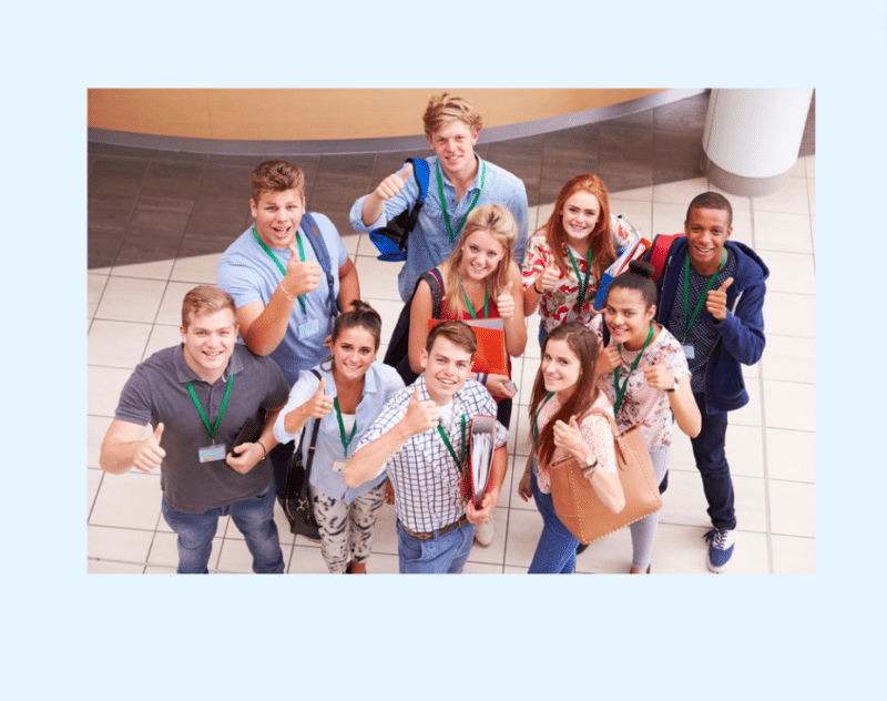 A group of students in a university hallway looking at a camera and giving thumbs up